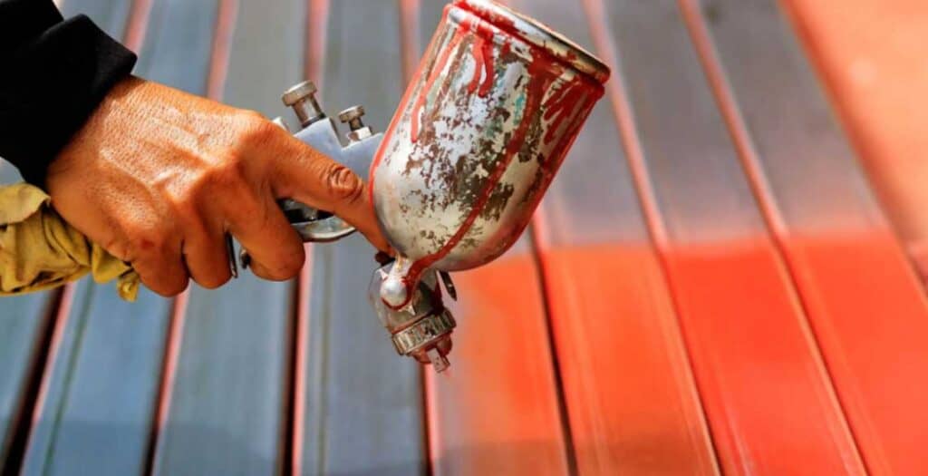Painting a garage door a bold orange color using a paint sprayer.